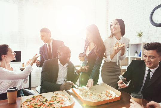 The office staff eat pizza and drink coffee in the business office.