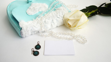 white rose, green earrings and turquoise bag on a white background
