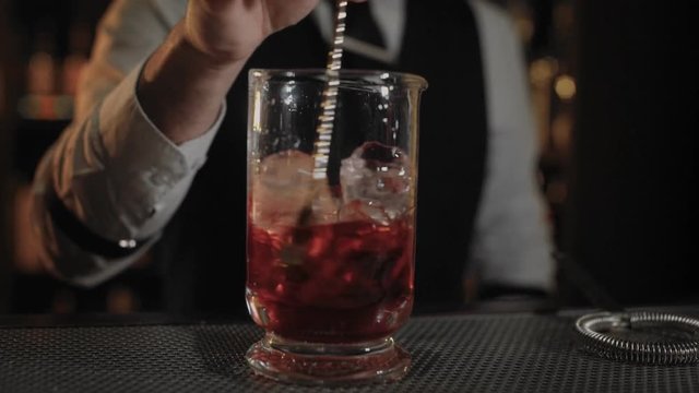 Moving shot on transparent glass vase filled with vermouth or rose wine and ice cubes, bartender is steering drink to cool down before mix it with other alcohol to prepare cocktail in restaurant bar.