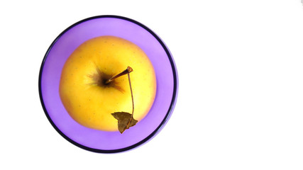 .yellow apple in a purple bowl on a white background