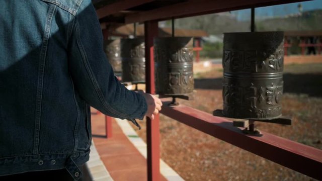Student or young traveller ot travel blogger turns buddhist prayer wheels at temple or sanctuary, prays to gods and spirits for good luck and success, superstition and cutural beliefs