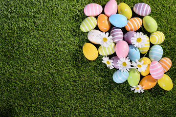 Fototapeta na wymiar above top view of multi colored painted easter eggs on green grass with springtime daisy flowers
