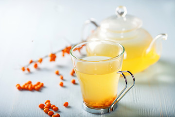 Vitaminic healthy sea buckthorn tea in small glass tea pot with fresh raw sea buckthorn berries. Selective focus