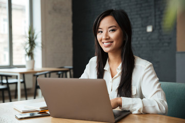 Cheerful young asian business woman using laptop