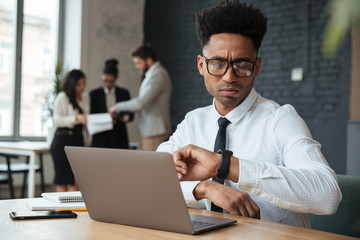 Concentrated young african businessman looking at watch.