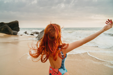 young red-haired woman with flying hair on the ocean coast at sunset, rear view
