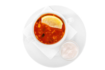 Solyanka, pickle with lemon and sour cream. On a napkin in a white plate isolated white. Serving dishes in a cafe, restaurant, for a menu. View from above