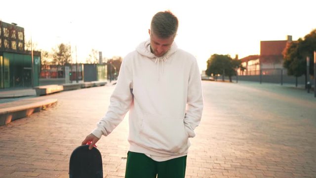 Cinemagraph of trendy hipster or millennial man or teenager stand in sunset light with skateboard and twist in his hand his board, concept cool lifestyle, forever young teen spirit