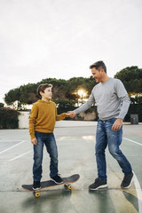 Father assisting son riding skateboard