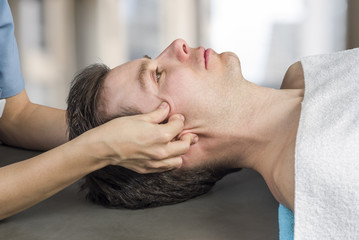 Physiotherapist, chiropractor doing a cranial sacral therapy to a man patient. Activating ...