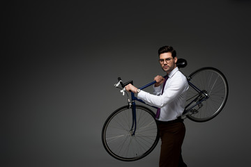 Young businessman in glasses holding bicycle in hands isolated on grey