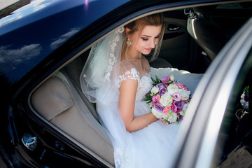 Happy charming bride sits in the black car