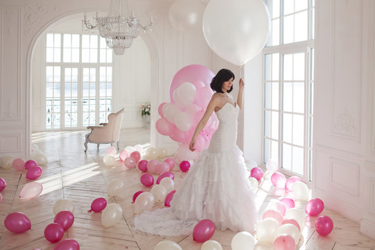 Young woman in wedding dress in luxury interior with a mass of pink and white balloons.