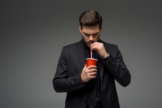 Young businessman drinking from disposable cup isolated on grey