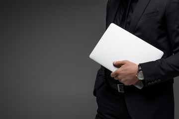 Partial view of businessman holding laptop in hand isolated on grey