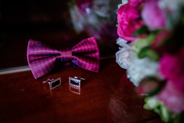 Pink bow tie, cufflinks and wedding bouquet lie on wooden table