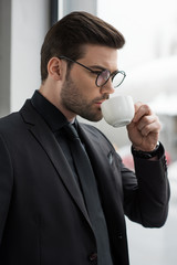 Side view of businessman in glasses drinking coffee