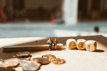 Miniature people, man and woman sitting with wooden number block and stack coins using as business and financial concept - Vintage filter