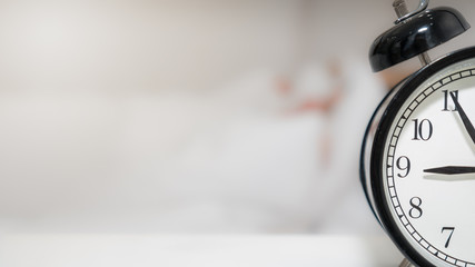 Alarm clock beside bed with blurred background of person in bed