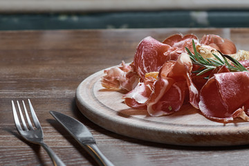 Wooden cutting board with prosciutto cheese on wooden table background.