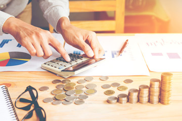 Businessman in grey shirt Hand holding ,Calculation with calculator and Financial data analyzing and counting on calculator in office on wood desk with light sunset background.