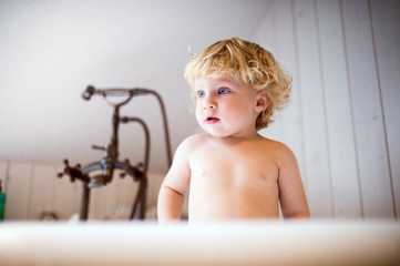 Cute toddler standing in the tub in the bathroom.
