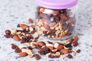 A mixture of nuts and raisins scattered on a table from a glass jar.