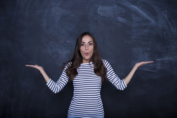 Thoughtful young woman looking at camera and keeping hands spread showing balance, standing against blackboard