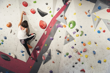 Woman practicing rock climbing on artificial wall indoors. Active lifestyle and bouldering concept.