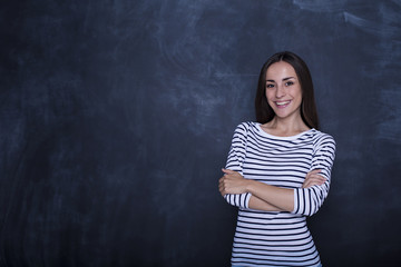 Attractive happy thoughtful woman looking on camera with crossed hands near copyspace over black background