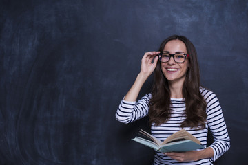 Study concept. Beautiful smiling woman with book on blackboard background