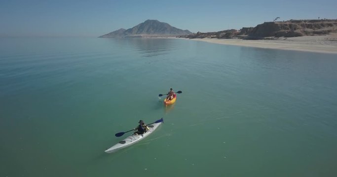 Aerial view of two women and a dog kayaking in a sea with a mountain in the distance.