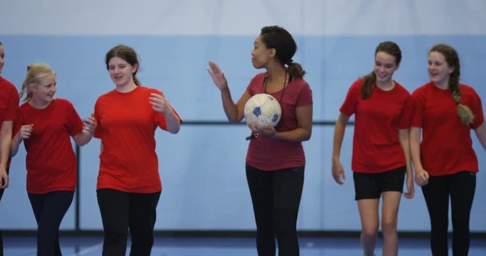 4K Female sports teacher coaching young female team on indoor soccer pitch