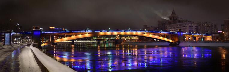 Brightly illuminated bridge at night in winter. Reflections in the river. Moscow. Urban landscape. Panoramic view.