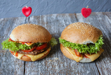 Tasty homemade cheeseburgers with mustard, tomatoes and green lettuce. Sesame burgers with red hearts on wooden background. Food photo with love.
