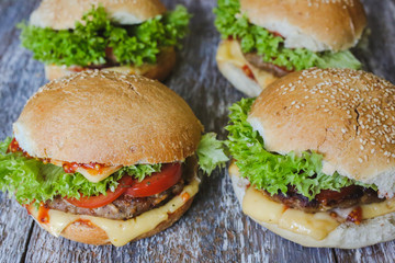 Tasty homemade cheeseburger with mustard, tomatoes and green lettuce. Sesame burgers on wooden background. Food photo.