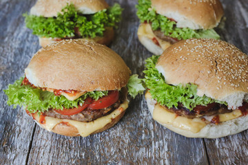 Tasty homemade cheeseburger with mustard, tomatoes and green lettuce. Sesame burgers on wooden background. Food photo.