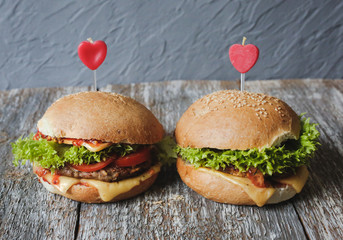 Tasty homemade cheeseburgers with mustard, tomatoes and green lettuce. Sesame burgers with red hearts on wooden background. Food photo with love.
