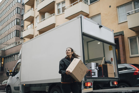 Woman carrying box while standing by delivery van in city