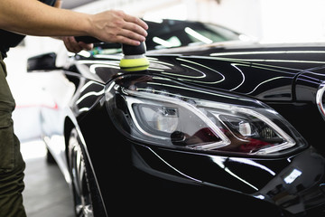 Fototapeta na wymiar Car detailing - Worker with orbital polisher in auto repair shop. Selective focus.
