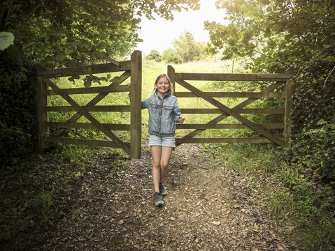 Full length of smiling girl standing by wooden gate on footpath amidst plants