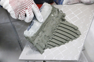 Repair - interior decoration. Laying of floor ceramic tiles. Men's hands tiler in gloves with  spatula spread  cement mortar on  ceramic floor tile.