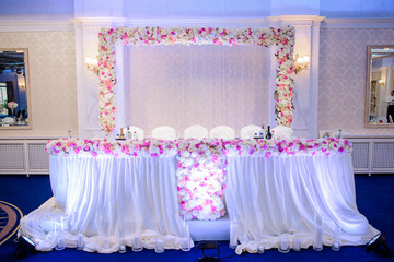 Colorful flower garlands made of white and pink roses decorate a place for wedding couple in the dinner hall