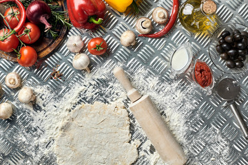 Ingredients and dough for making pizzas with an overhead view on freshly mixed mounds of pastry, a jar of olive oil and pot of tomato sauce, overhead view