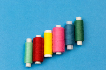 Coils with multi-colored threads on a blue background. Threads for sewing different colors are arranged in steps on a blue background.