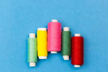 Coils with multi-colored threads on a blue background. Threads for sewing different colors are arranged in steps on a blue background.