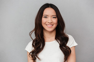 Portrait of asian lovely woman with dark curly hair posing with kind smile, isolated over gray background - Powered by Adobe