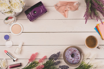 top view of flowers, camera, cosmetics, cup of coffee and doughnut on wooden table top