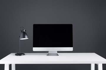 modern desktop computer with blank screen and lamp on table at workspace
