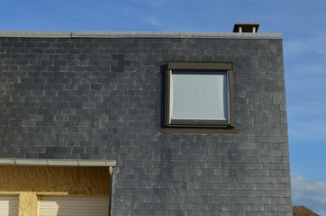 Maison avec façade en ardoises et fenêtre de toit. (France)